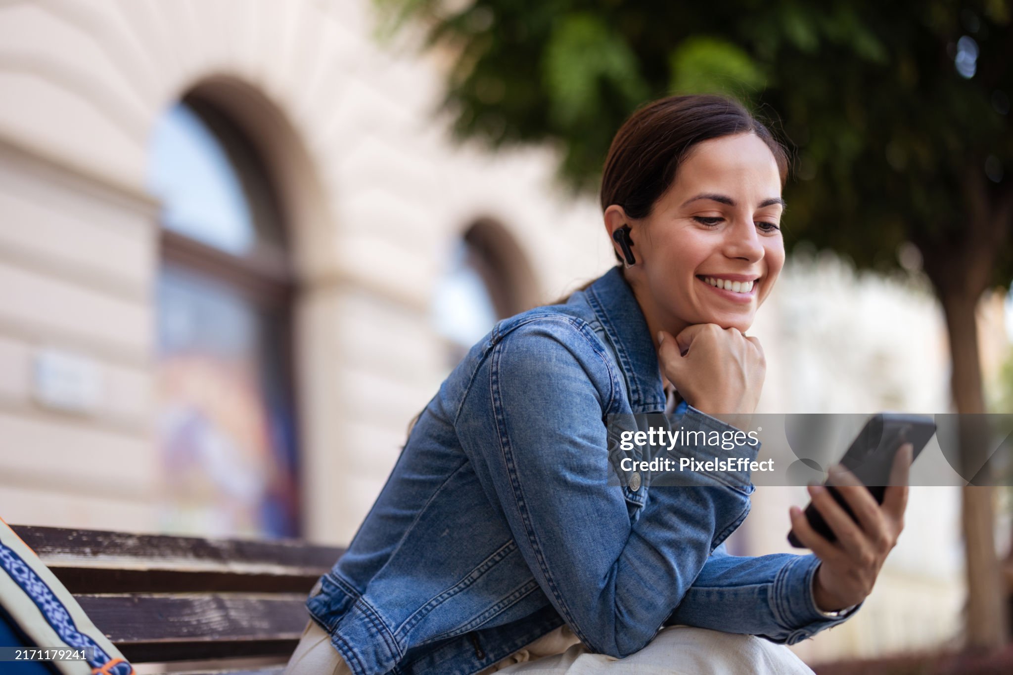 Relaxed Woman Listens to Music With Wireless Earbuds and Mobile Phone in the City Center